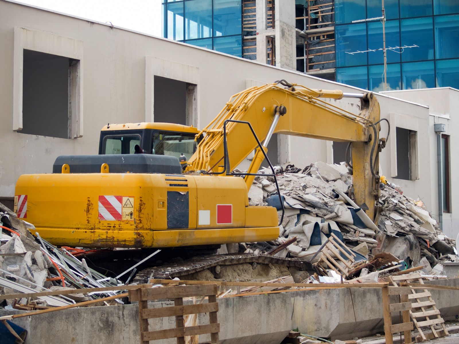 A yellow excavator is demolishing a building on a construction site.
