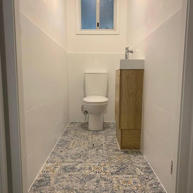 A Washroom With A Closed Toilet Seat And Window Above — Bridge Plumbing & Trades in Nowra, NSW