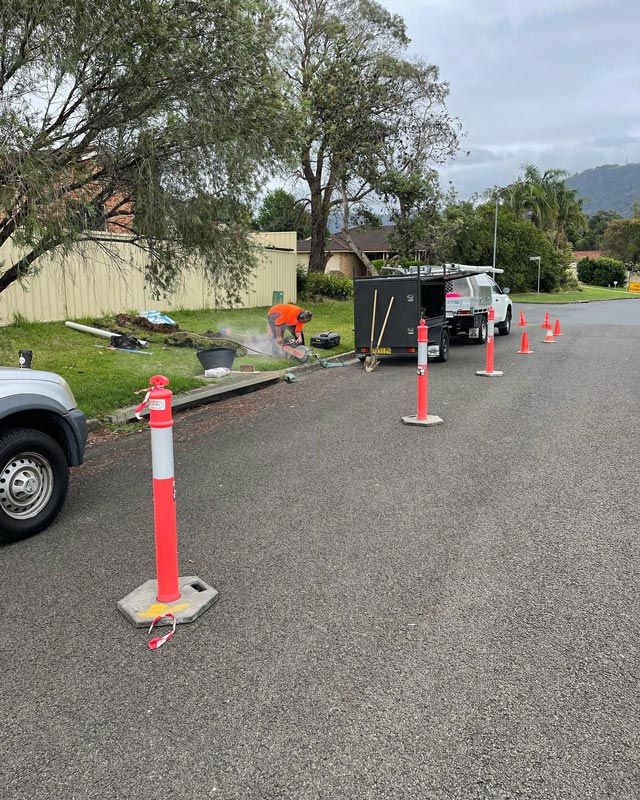 A Man In Orange T-Shirt Repairing A Drain On A Road Side — Bridge Plumbing & Trades in Nowra, NSW