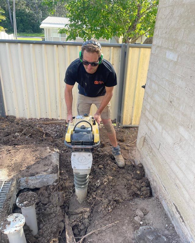 A Man In Black T-Shirt Drilling In The Ground — Bridge Plumbing & Trades in Nowra, NSW