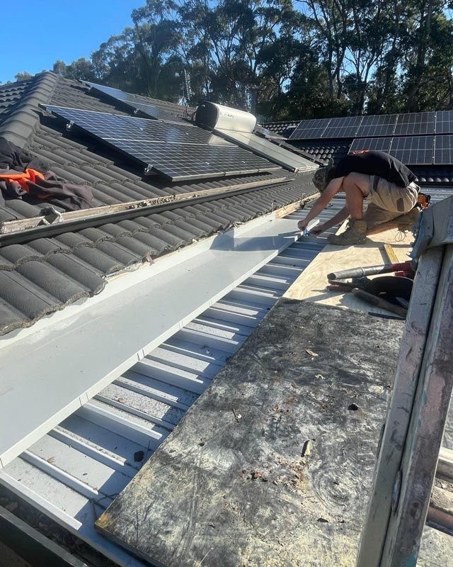 A Man In Black T-shirt Fixing A House Roof — Bridge Plumbing & Trades in Nowra, NSW