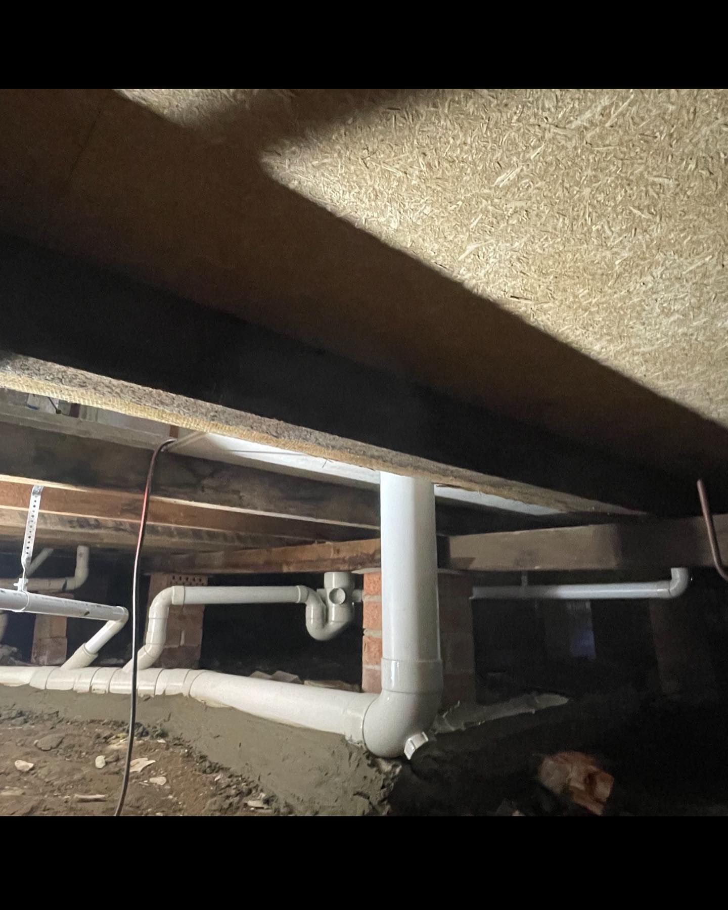 White Plumbing Pipes Run Along Wooden Beams and Brick Supports — Bridge Plumbing & Trades In Jervis Bay, NSW