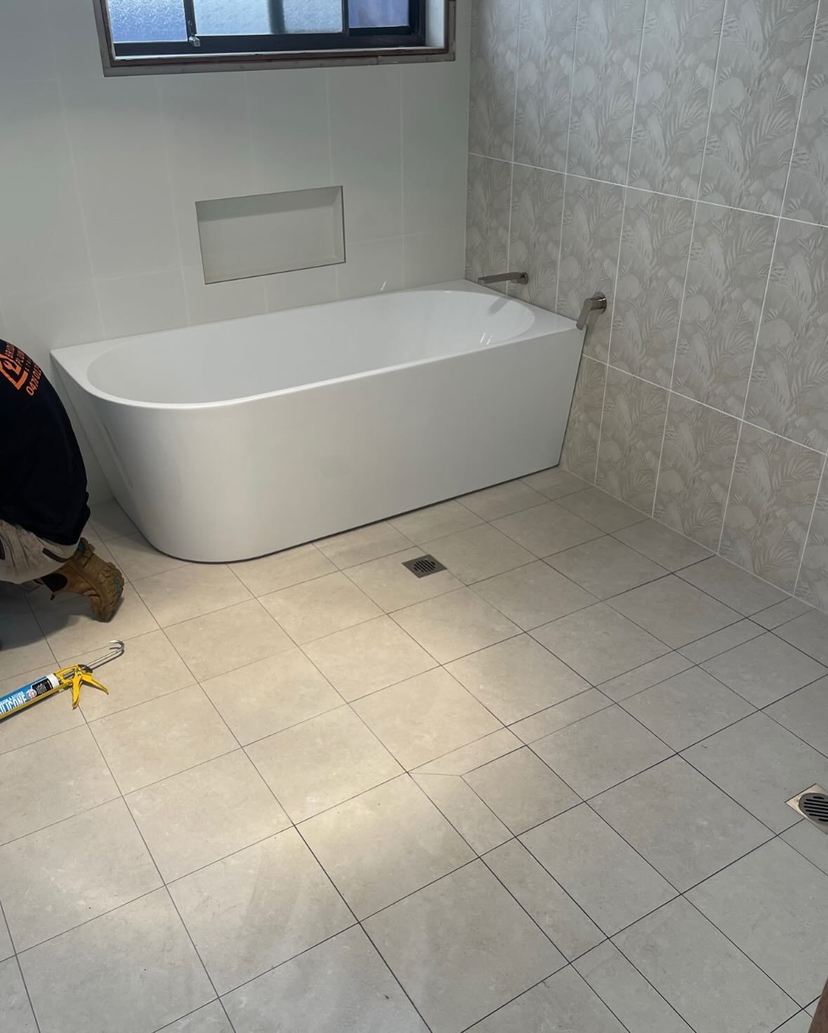 A Man is Kneeling in a Bathroom Next to a Bathtub — Bridge Plumbing & Trades in Nowra, NSW