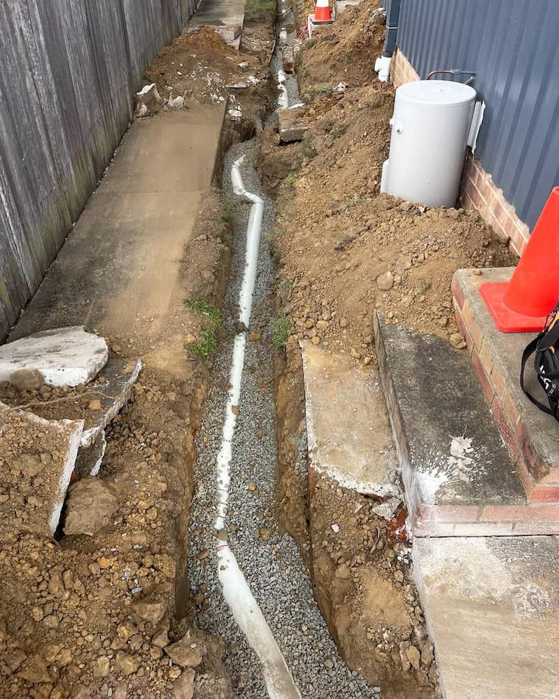 A Drain Pipe is Being Installed in the Dirt Next to a Fence — Bridge Plumbing & Trades in Nowra, NSW