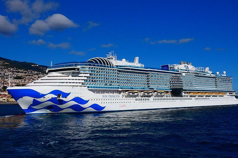 Large white cruise ship with blue wave graphics sailing on a calm blue sea under a clear sky