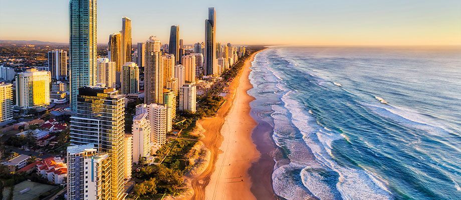 High-angle view of a coastal city with tall buildings and a beach, ocean waves, and a golden sky.