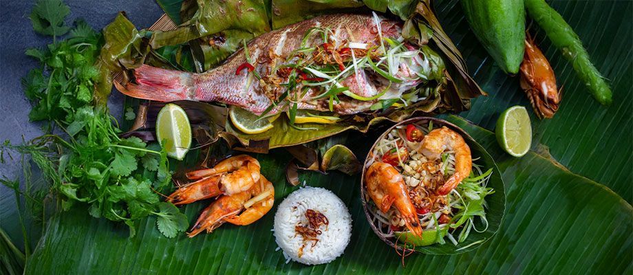A dish of whole baked fish, shrimp, rice, and lime on a banana leaf.