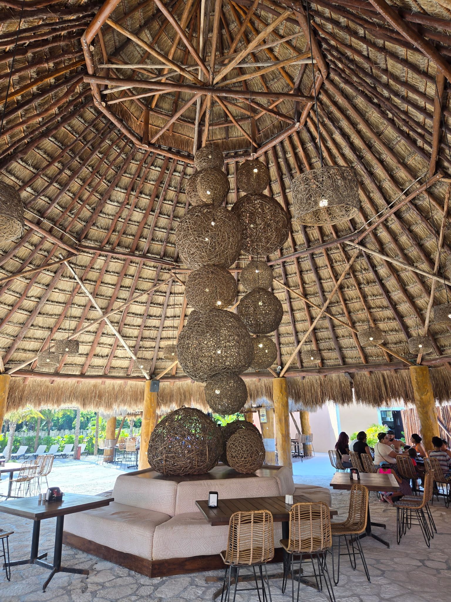 Gazebo-style outdoor dining area with thatched roof, decorative sphere lights, and tables with patrons.