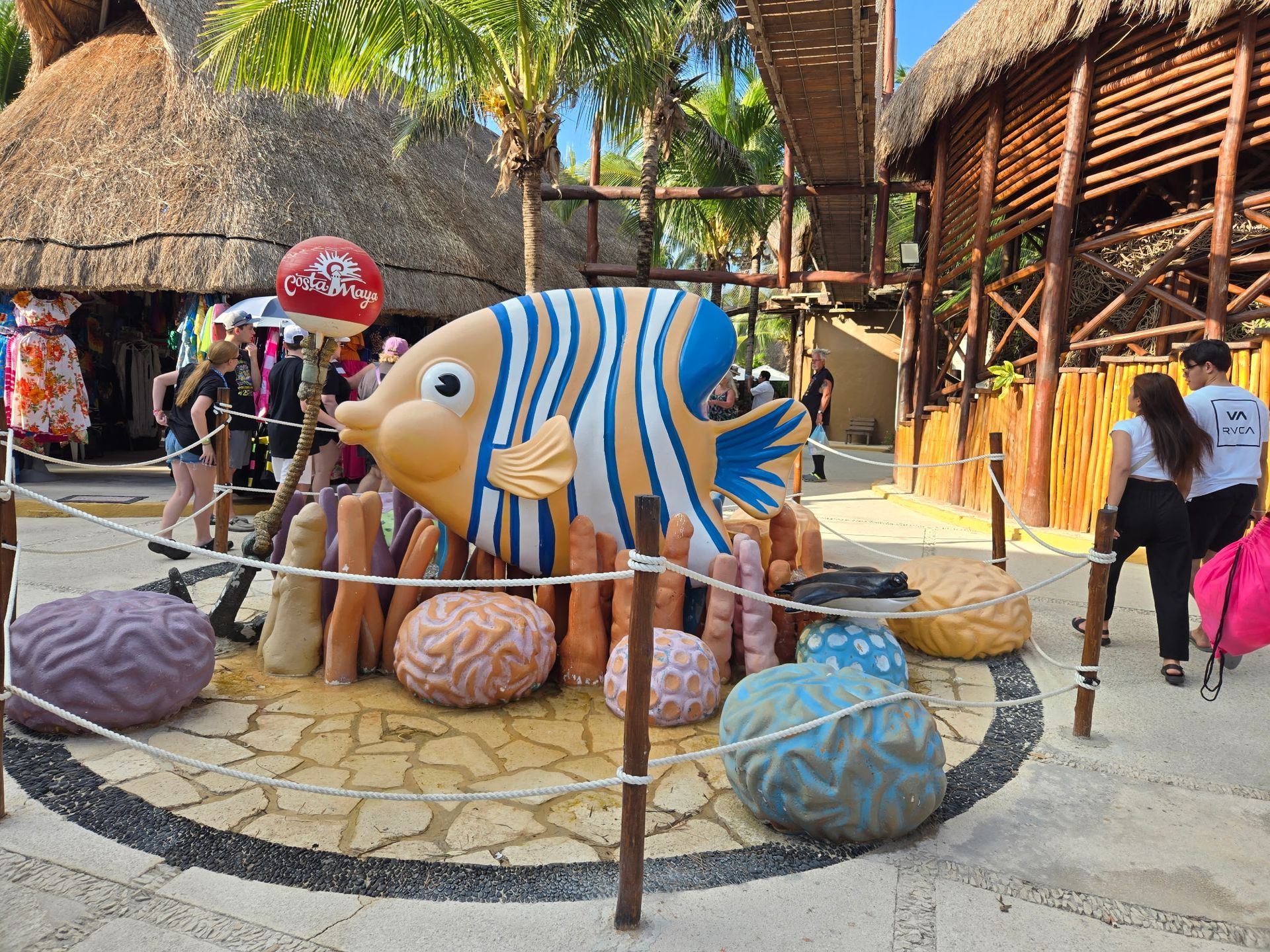 Large colorful fish sculpture with coral and people in a tropical setting.