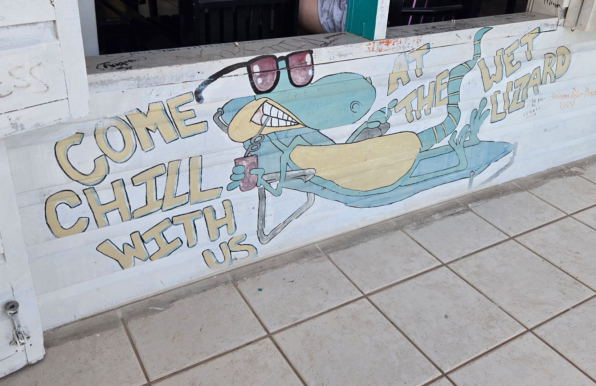 Mural on white wall: turquoise cartoon shark wearing sunglasses, holding drink; text says 
