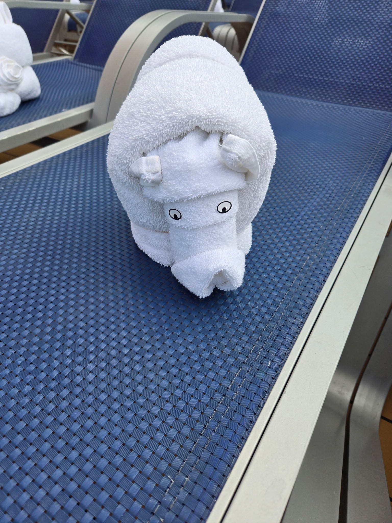 Towel animal shaped like a polar bear on a blue lounge chair, with a ship's rail in background.