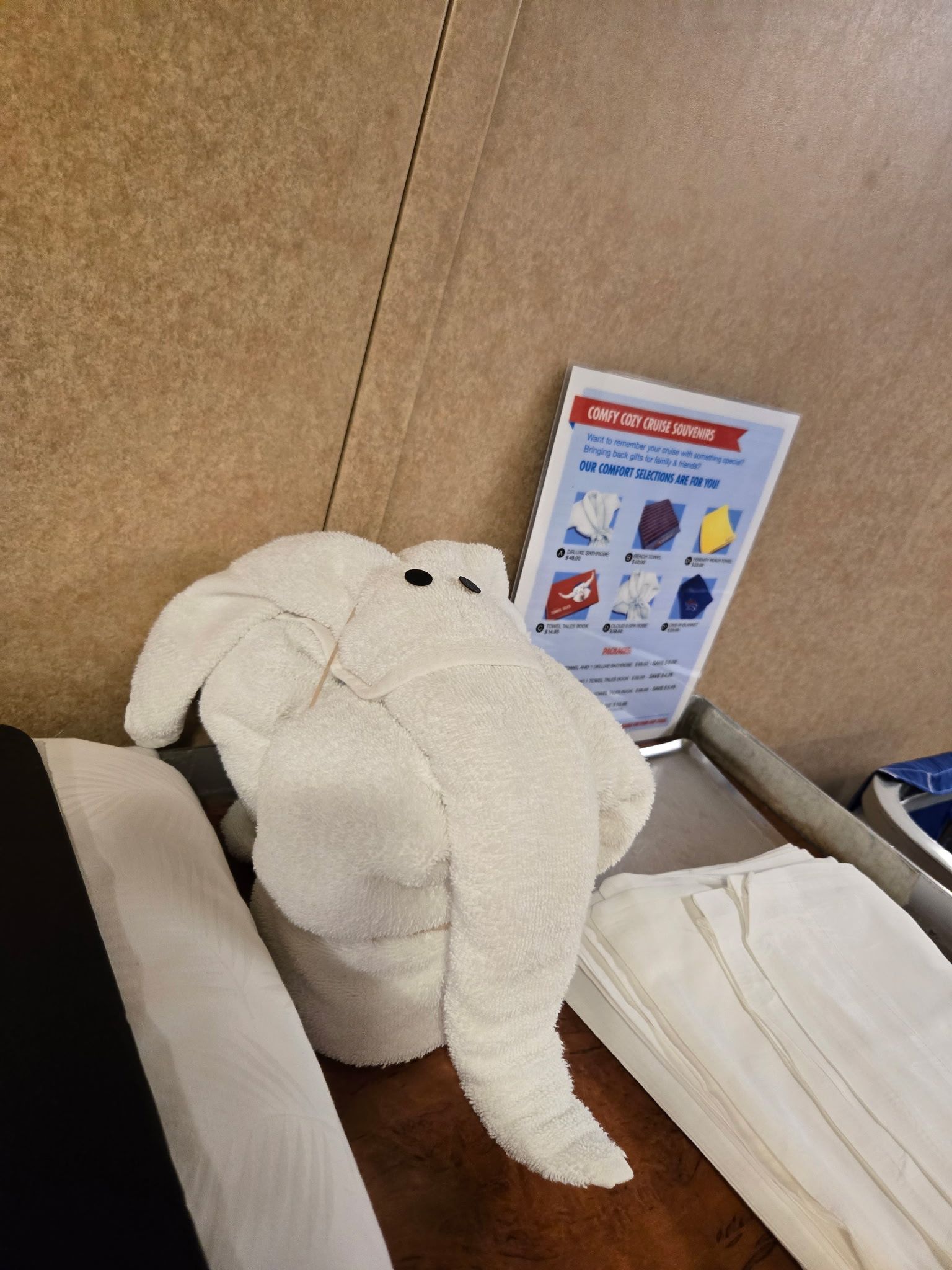 White towel elephant sitting on a tray with a pamphlet, brown background.