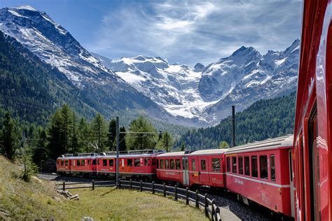 Red train curving through alpine valley with snowy mountains and forest backdrop