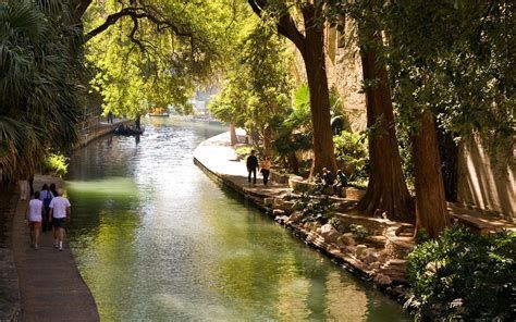 Tree-lined river canal with people walking along the banks in sunlight
