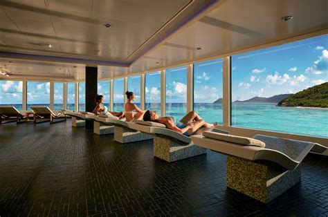 People lounging on sunbeds in a bright spa overlooking a turquoise ocean and islands.