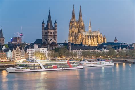 Cologne Cathedral and city skyline lit at dusk along the Rhine River with a docked boat