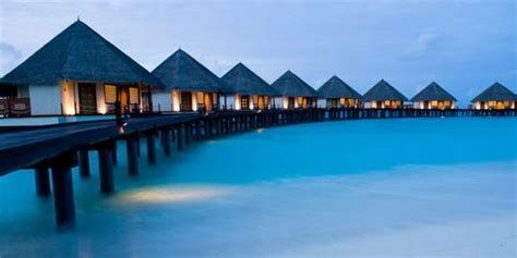 Overwater bungalows on a turquoise lagoon at dusk, with warm lights glowing along the pier.