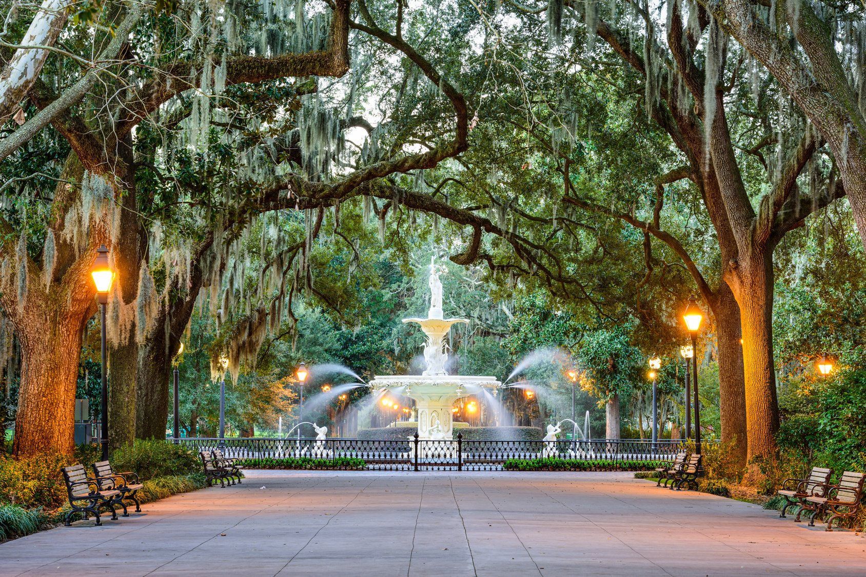 A fountain in a park surrounded by trees and benches.