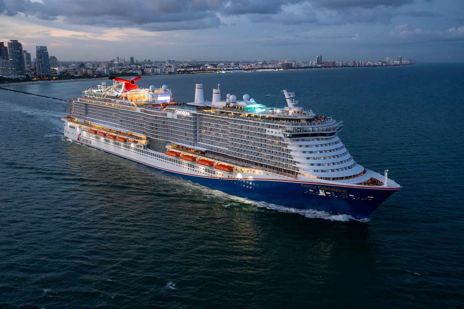 Large white cruise ship sailing near a city coastline at dusk