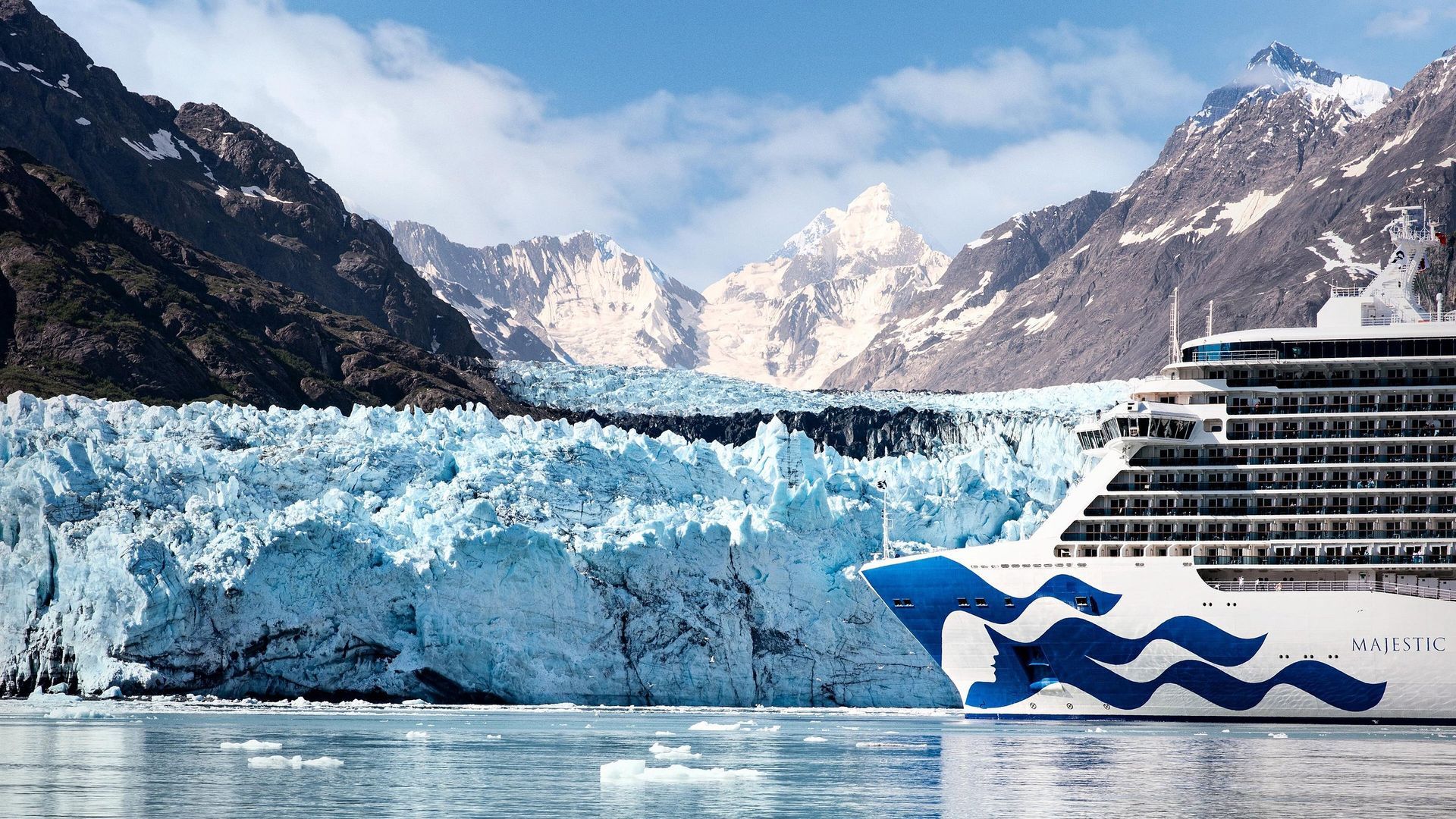 A Princess cruise ship sailing in front of a massive, blue glacier set against snow-capped mountains.
