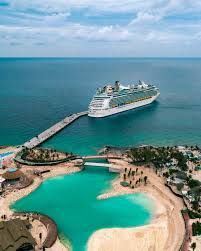 Cruise ship docked at a tropical resort with turquoise water, sandy beach, and a long pier under a blue sky