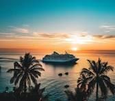 Cruise ship at sunset with palm trees framing a calm tropical harbor