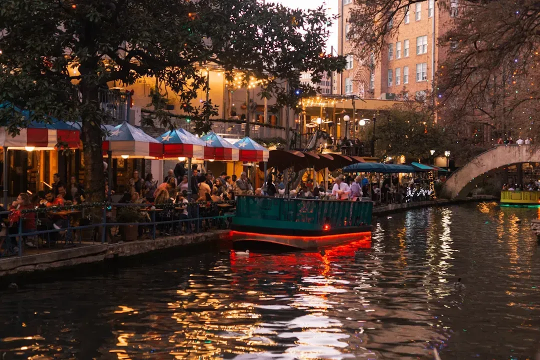 A boat is floating down a river in a city at night.