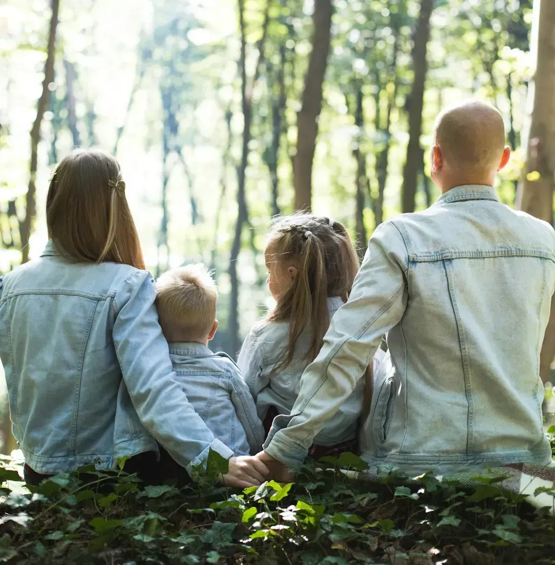 A family is sitting in the woods holding hands and looking at the trees.