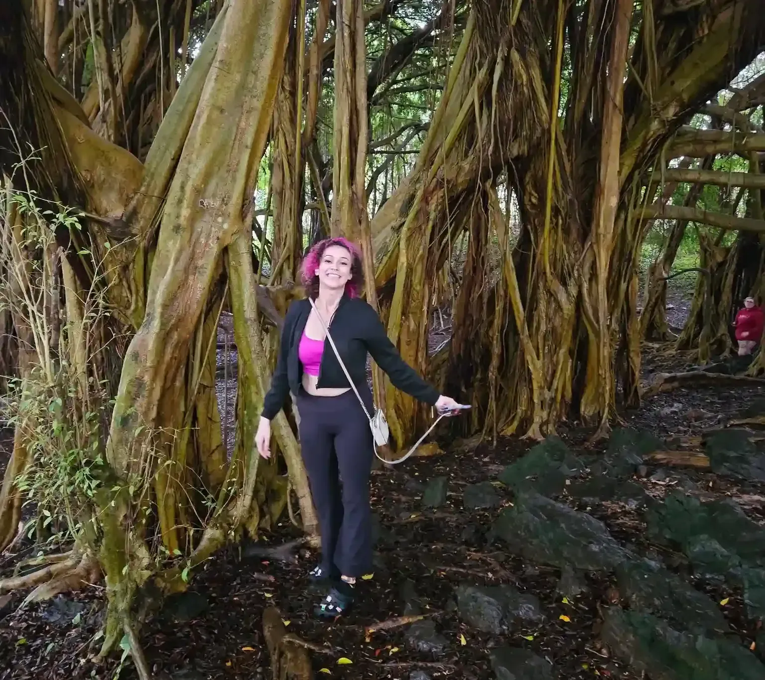 A woman with pink hair is standing under a tree