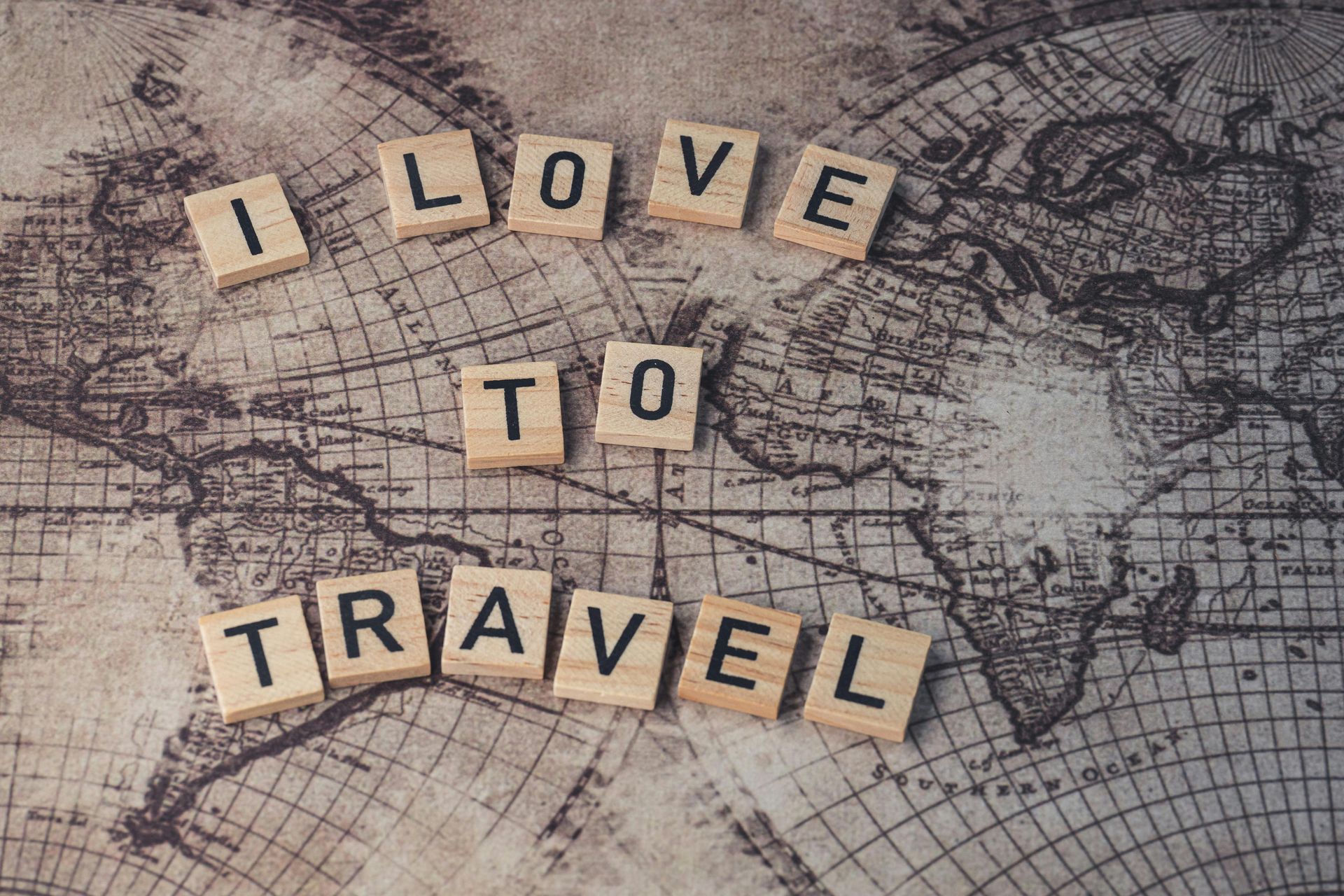 Scrabble tiles spelling “I LOVE TO TRAVEL” on a vintage world map background