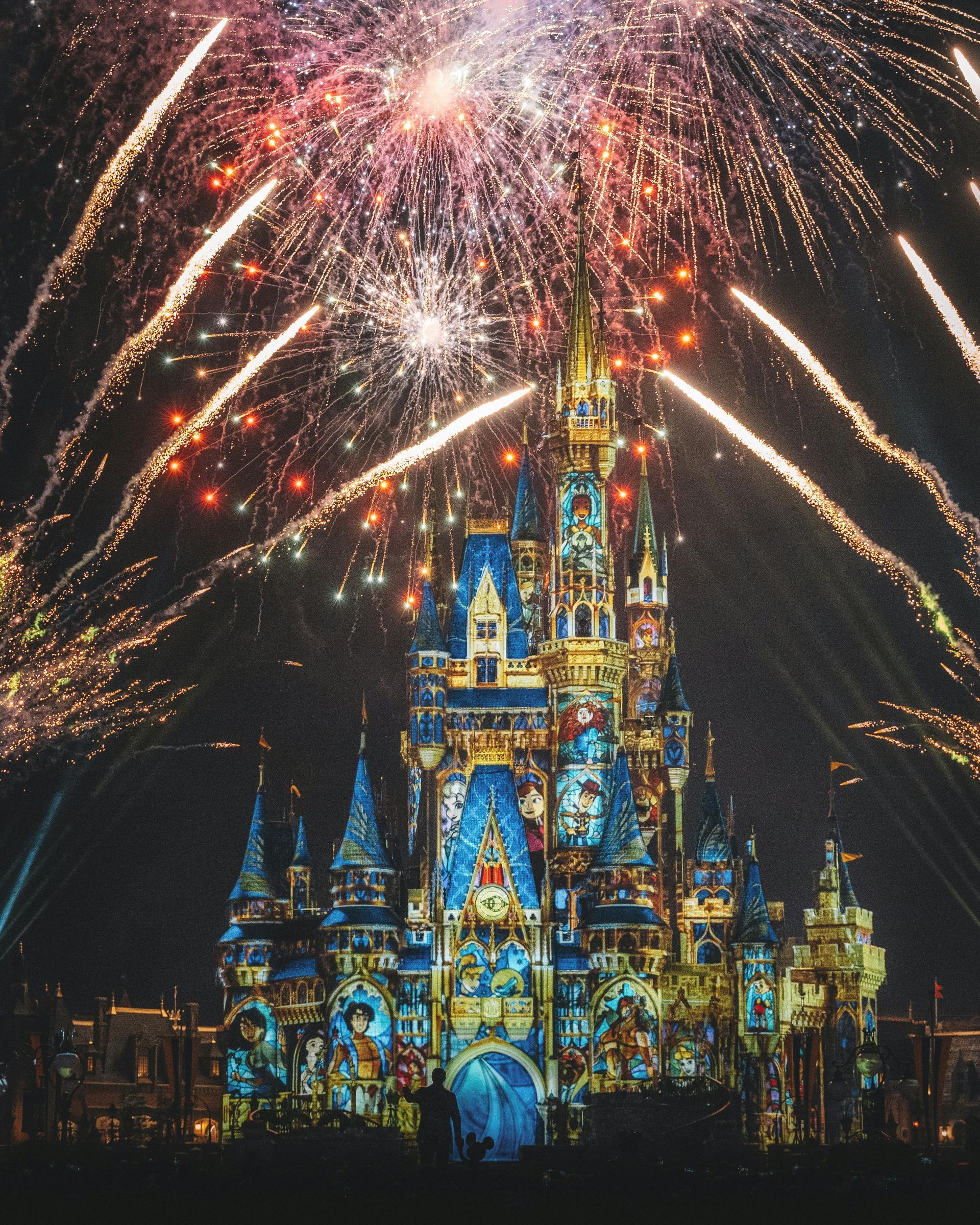 Fireworks bursting above a brightly lit fairy-tale castle at night
