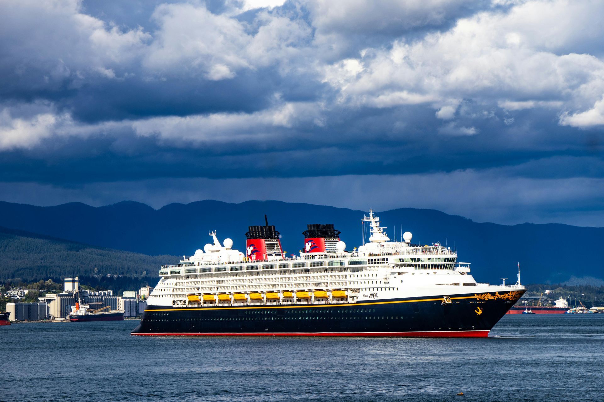 Large white-and-red cruise ship on calm water with cloudy mountains in the background