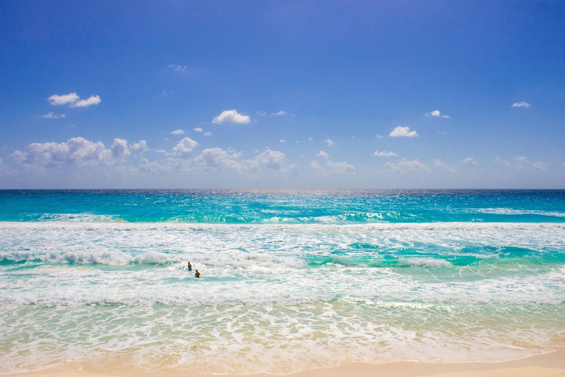 Sunny beach with turquoise waves, white sand, and a blue sky with small clouds