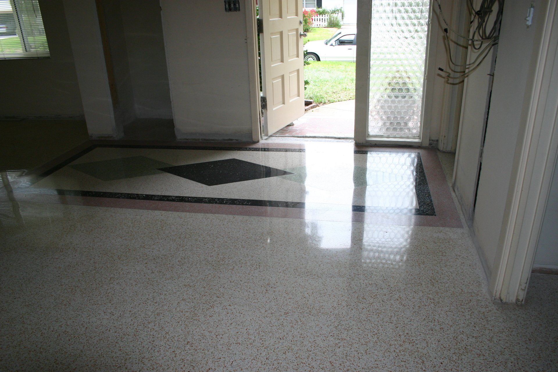Polished terrazzo flooring with a dark geometric inlay border in a residential entryway leading to an open doorway.