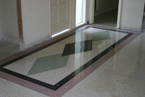 A polished stone floor features a rectangular border in black and pink with three inlaid diamond shapes in green and black.