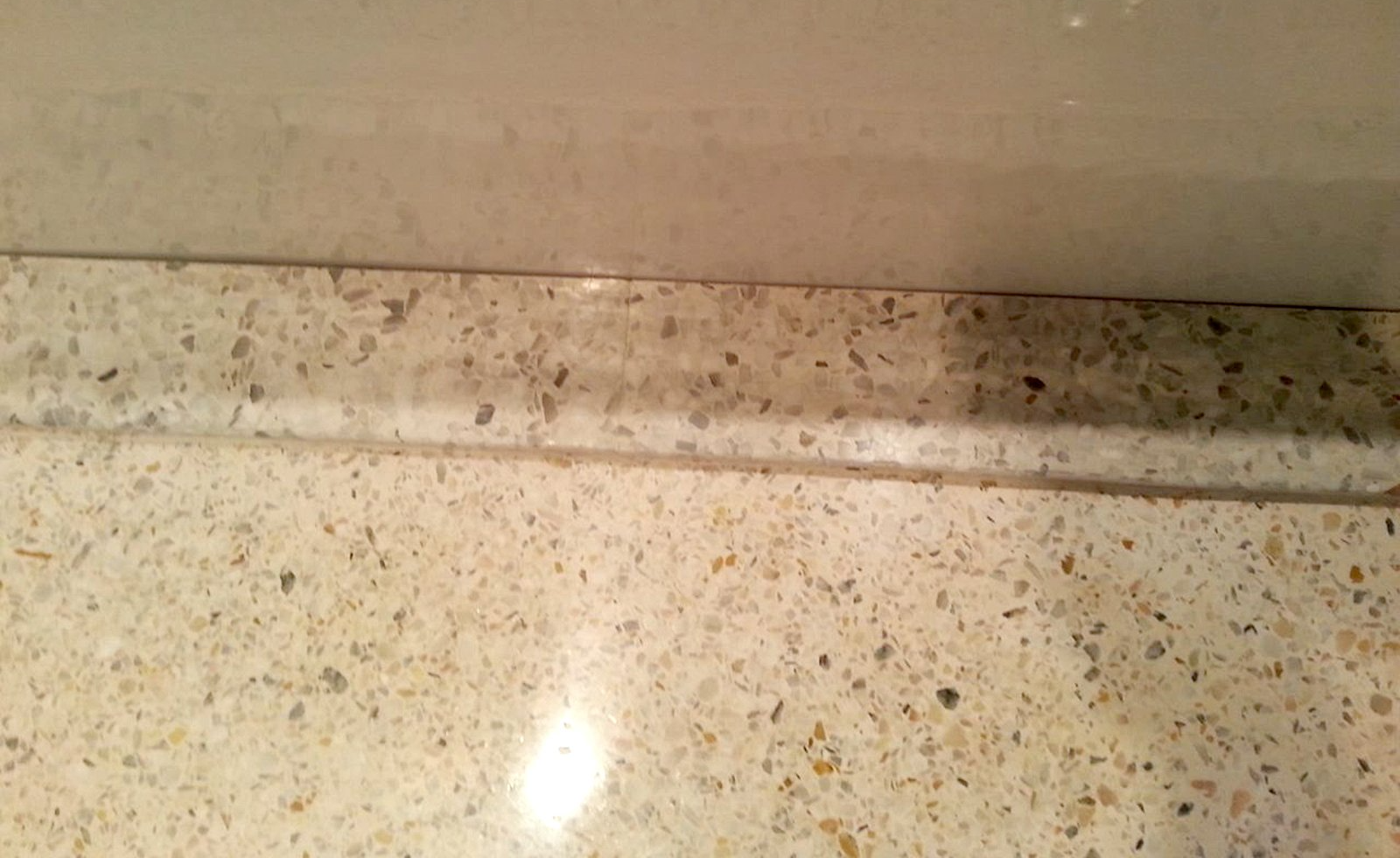 A light beige, speckled stone countertop meets a wall with a matching stone backsplash trim.