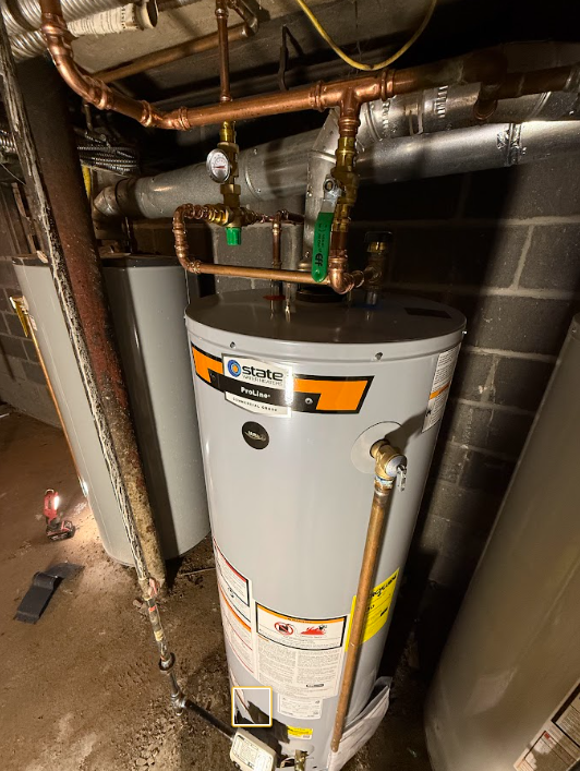 Water heater in a cramped utility closet with exposed pipes and a cinderblock wall
