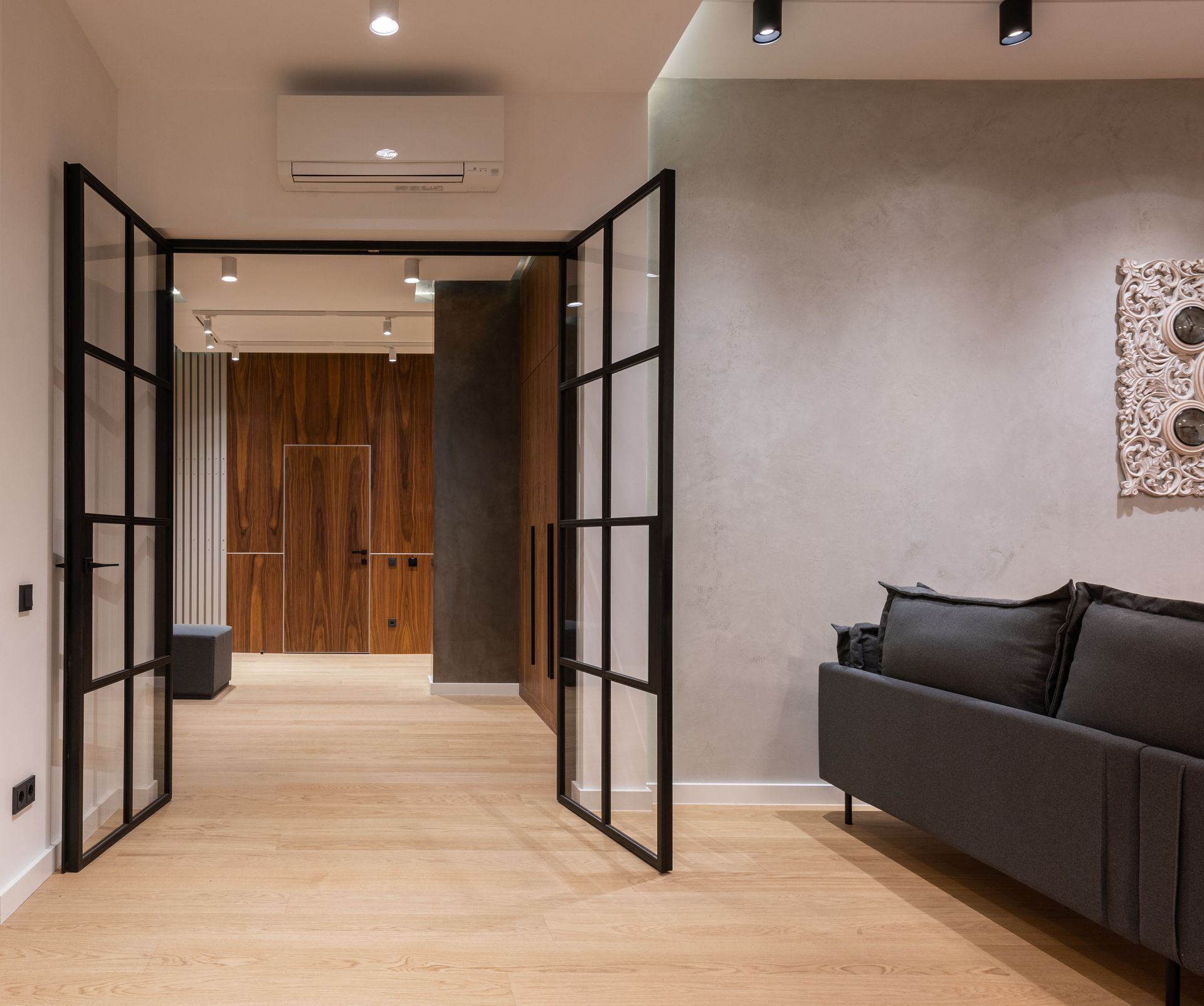 Modern living room with open black-framed glass doors, wood floor, gray sofa, and wall art