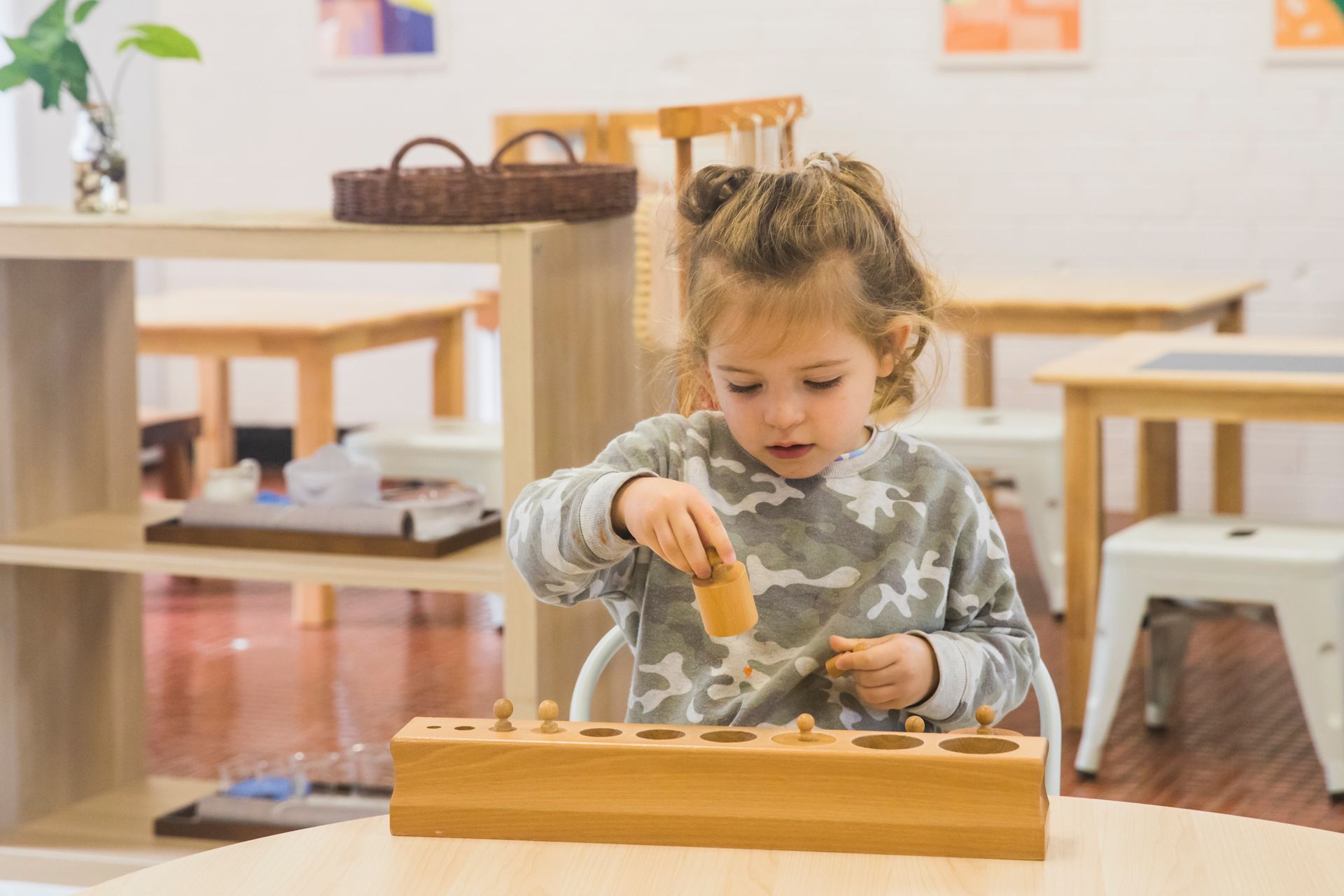 A little girl is sitting at a table playing with a wooden toy.