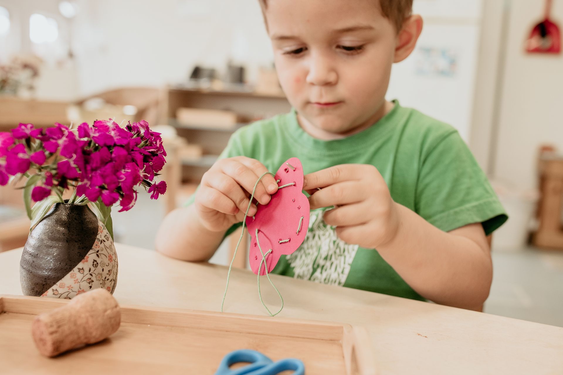 A young boy is sitting at a table cutting a piece of paper with scissors.