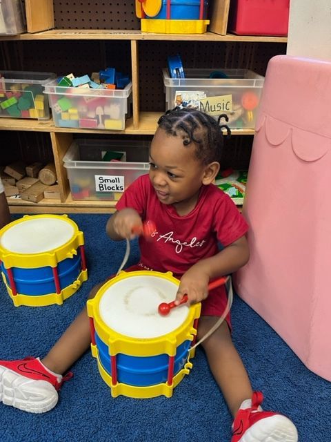 A little girl in a red shirt is playing a toy drum