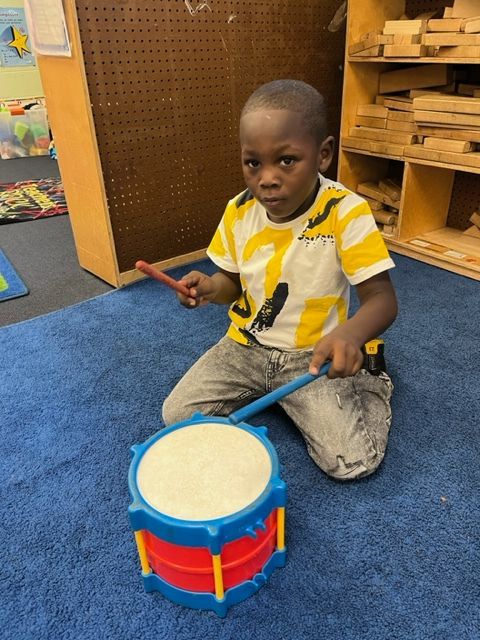 A young boy is kneeling on the floor playing a toy drum
