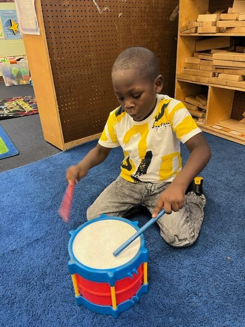 A young boy in a yellow and white shirt is playing a toy drum