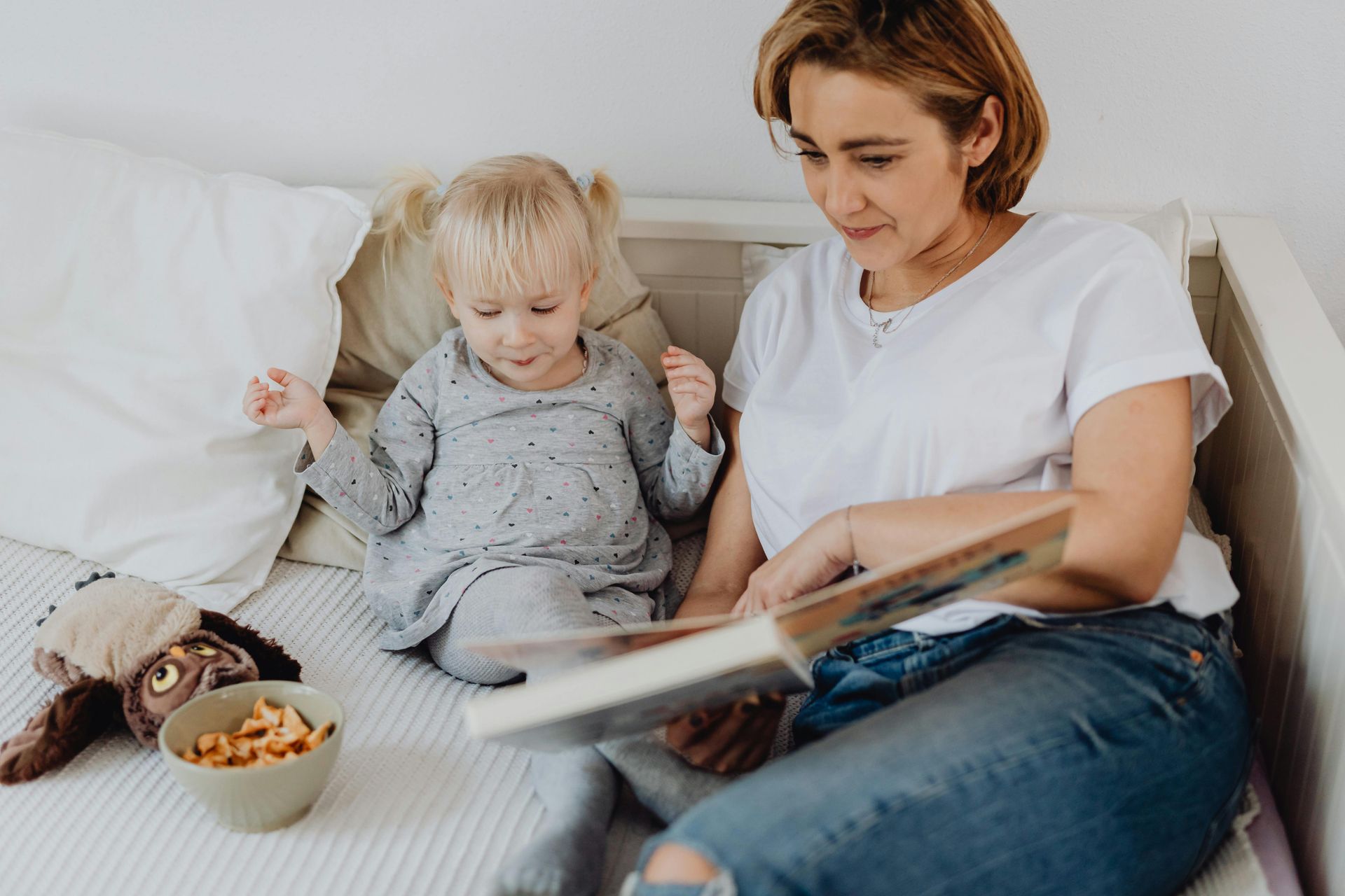 A woman is sitting on a bed reading a book to a little girl.