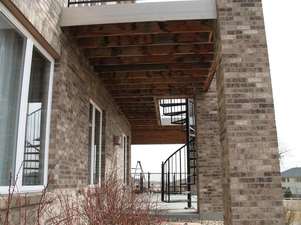 Covered outdoor patio with a concrete floor, stone columns, and wood beams.
