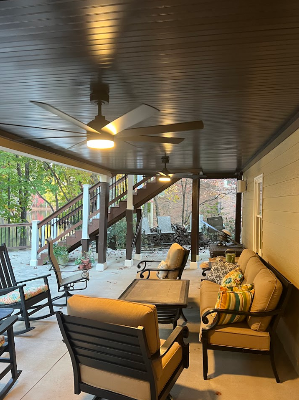 Outdoor patio with seating, ceiling fans, and a staircase. Brown ceiling and furniture, tan wall.