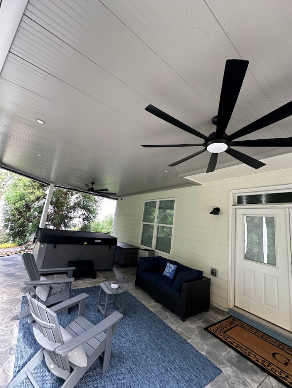 Covered patio with a hot tub, seating, and a ceiling fan.