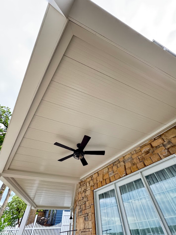 Beige patio ceiling with dark ceiling fan, next to a stone wall and windows.