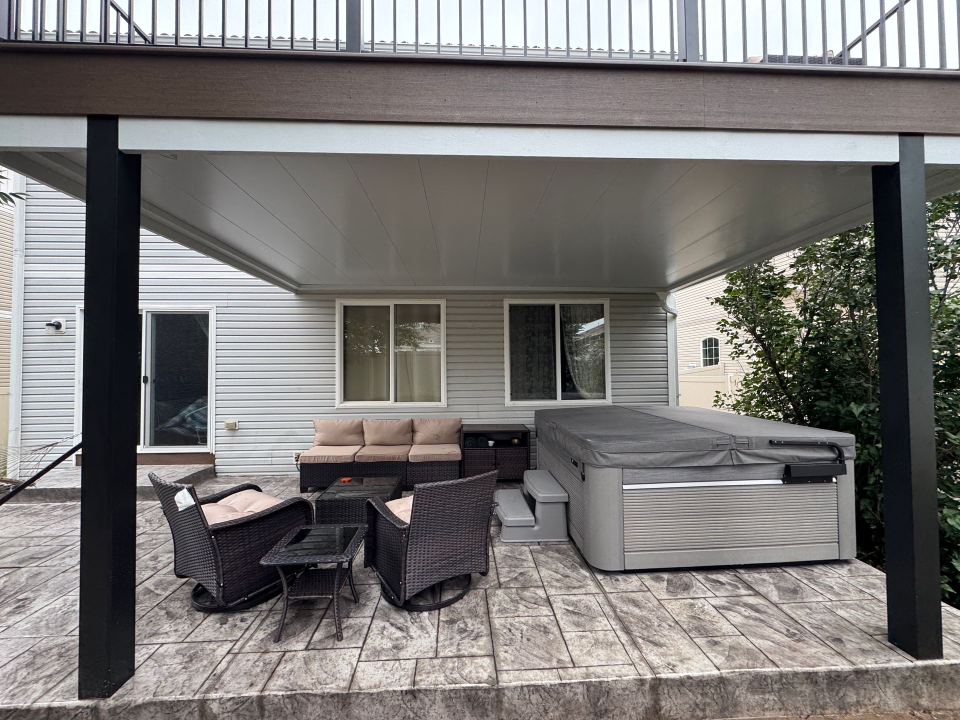 Patio with seating, hot tub, under a deck. Black posts support the roof.