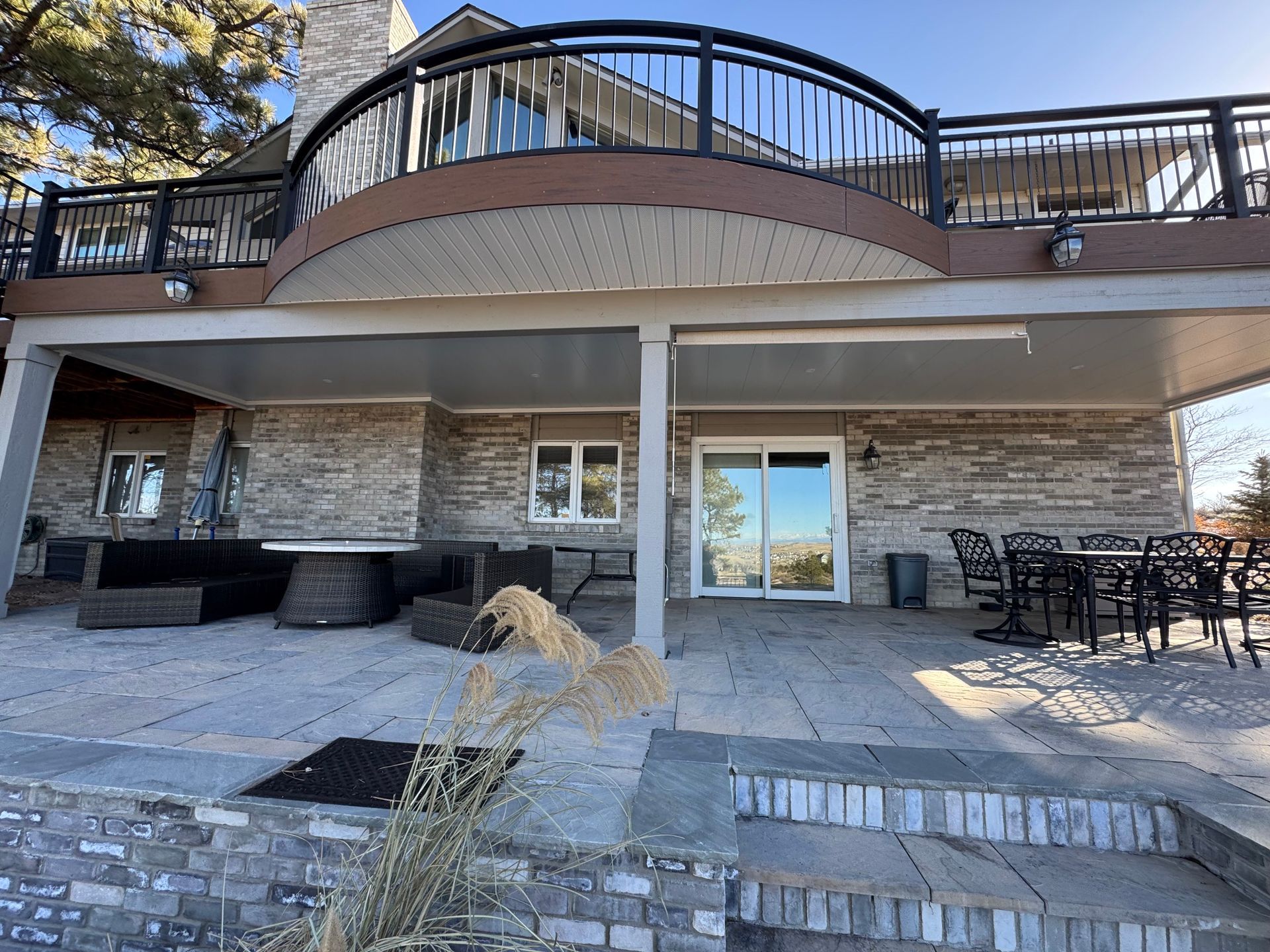 Stone patio with outdoor furniture beneath a large balcony with black railing.